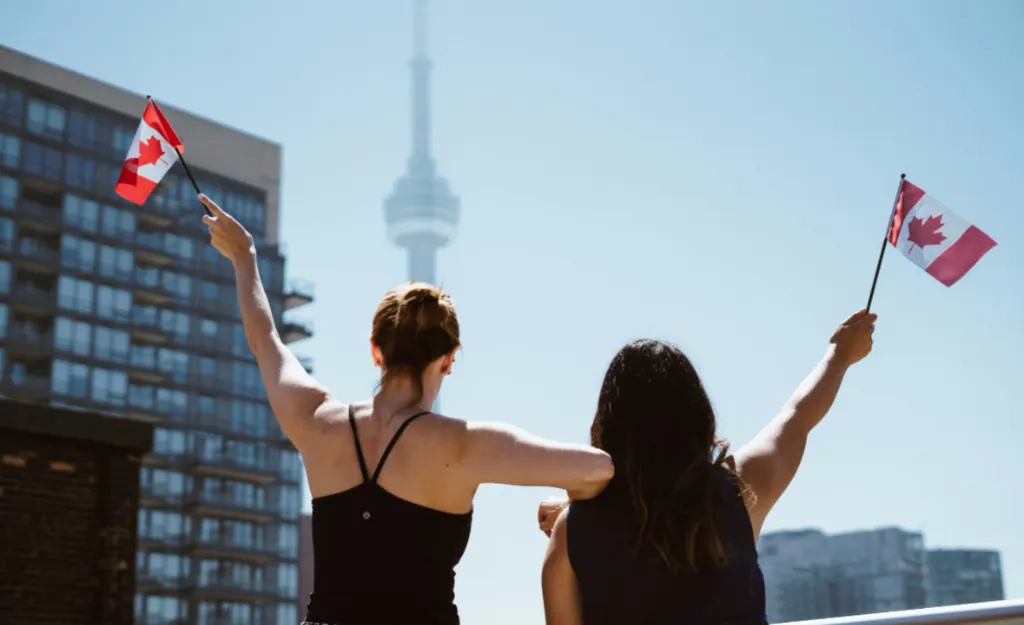 Deux expatriées brandissant des drapeaux canadiens devant la tour CN à Toronto